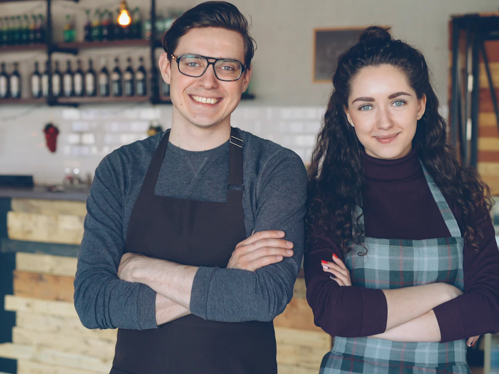 Two proud small-business owners standing with arms crossed in their café